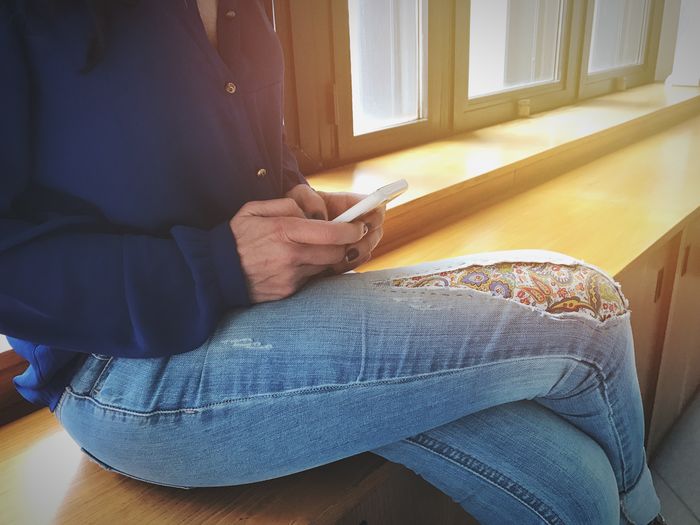 Midsection of woman using mobile phone while sitting on window sill