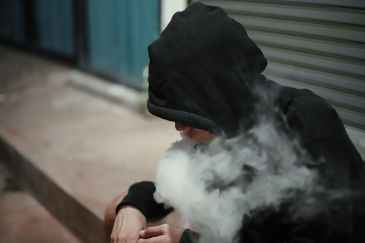 Man smoking while sitting on footpath