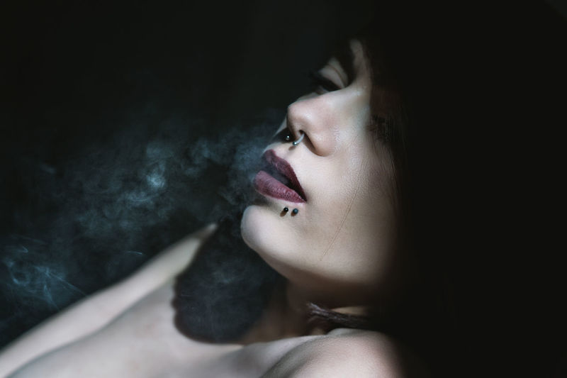 Close-up of sensual woman exhaling smoke in darkroom