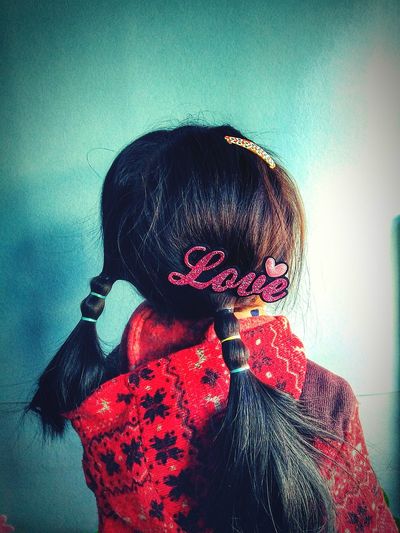 Rear view of girl with pigtails and love clip in hair while standing against wall