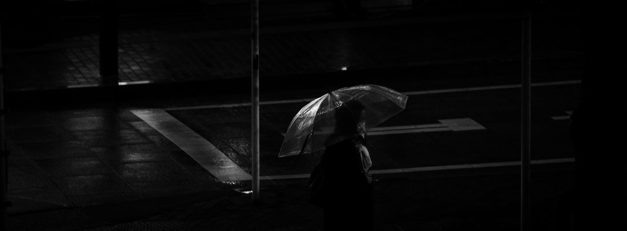 Woman wearing mask holding umbrella while standing on road at night