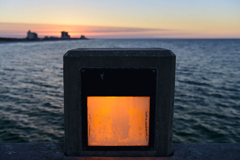 Close-up of fire on sea against sunset sky