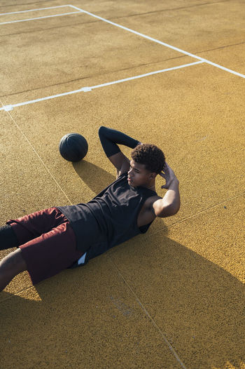 African american sportsman in uniform doing crunches on yellow marked playground with ball in bright day