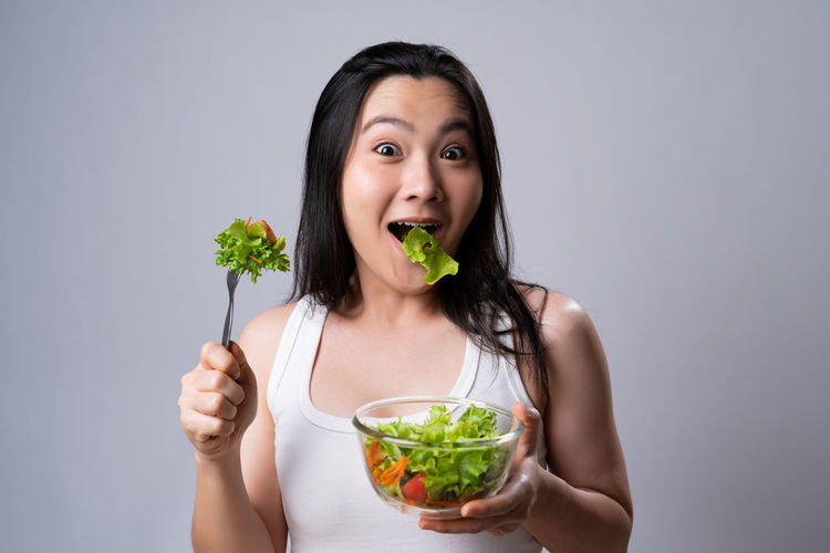 Portrait of young woman eating food against white background