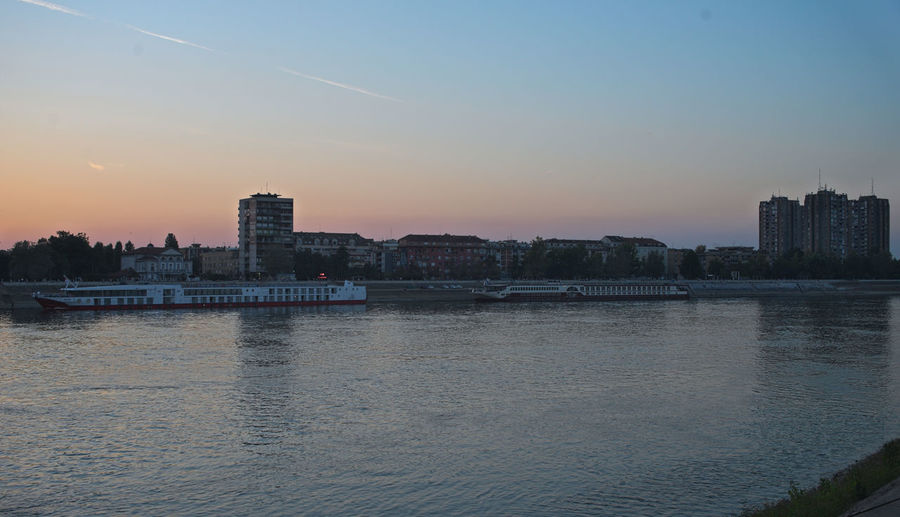 Scenic view of river by buildings against sky at sunset