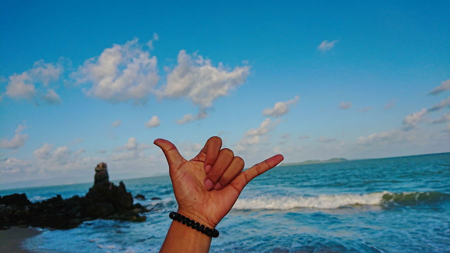 Cropped image of person gesturing by sea against sky