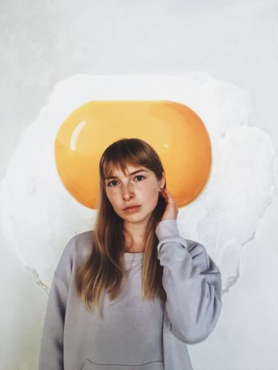 Portrait of young woman standing against fried egg poster on wall
