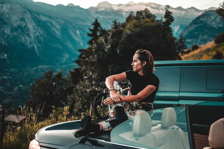 Woman sitting on car against mountains
