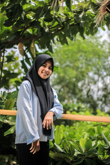 Portrait of smiling woman standing against trees