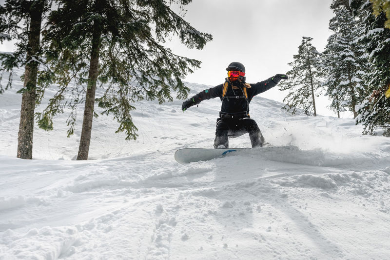 Woman on a snowboard in a helmet quickly descends from the ski slope in the middle of the forest