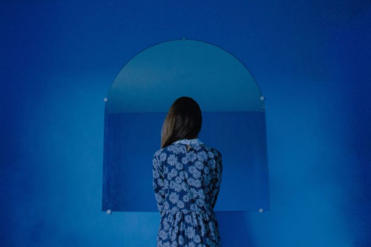 Rear view of woman standing against mirror on blue wall