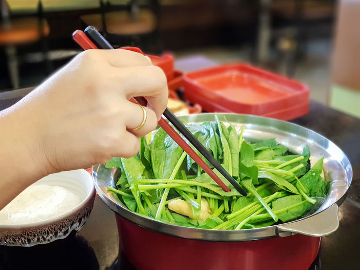 Cropped hand holding vegetables with chopsticks