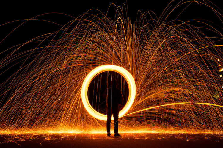 Silhouette man spinning wire wool on field at night