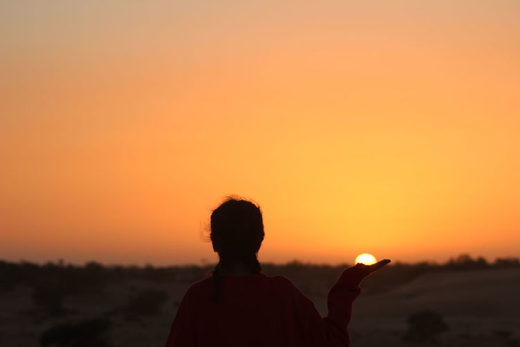 Optical illusion of woman holding sun against sky during sunset