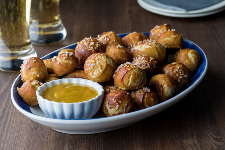A platter of homemade pretzel bites with mustard dip and beer in behind.