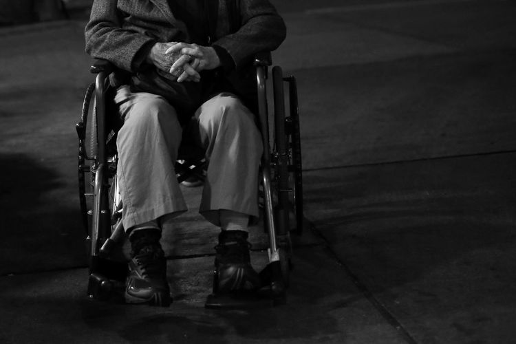 Low section of man with hands clasped sitting on wheelchair