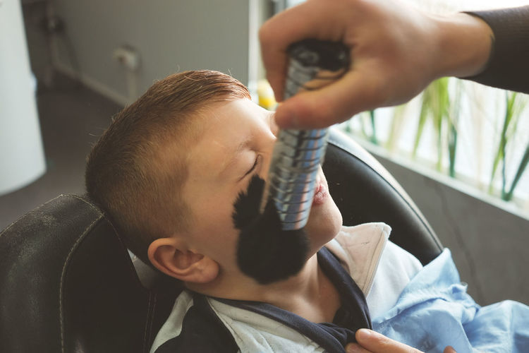 Cropped image of man brushing on boy face at hair salon