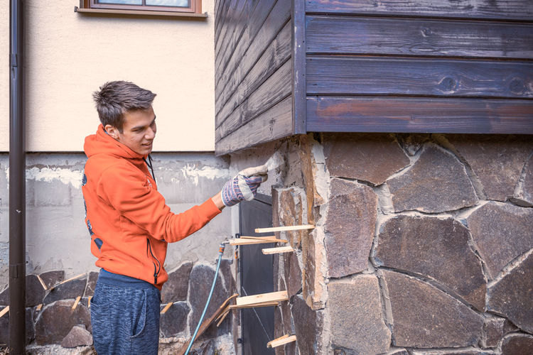 Side view of young man repairing stonewall outdoors