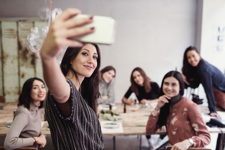 Smiling young woman taking selfie with female coworkers at workshop