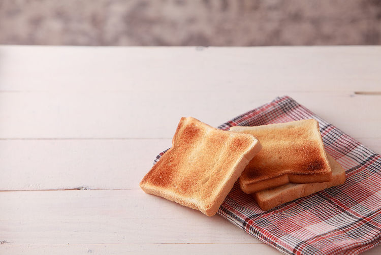 A stack of sliced bread toasts on white wooden background