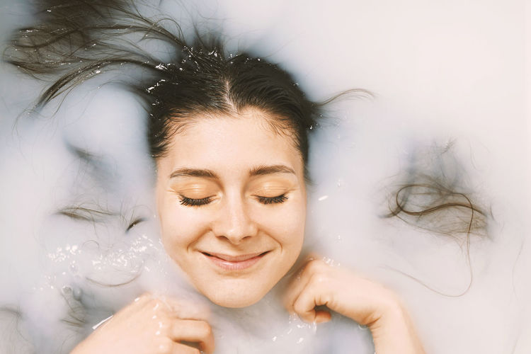 Young woman taking a bath in milk - happy with closed eyes - self care and wellbeing concept