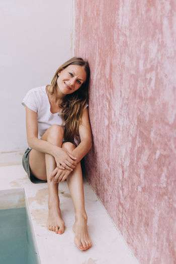 Portrait of young woman sitting against wall next to a pool