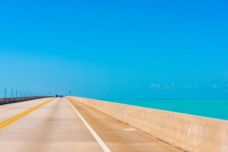 Road by sea against clear blue sky