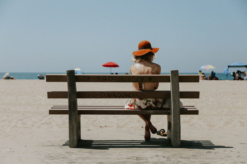 Rear view of woman sitting on bench at beach
