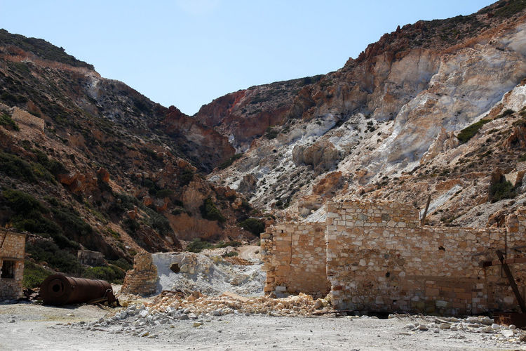 Abandoned sulfur mine in the greek coast with a rusted and weathered silo next to the red cliffs
