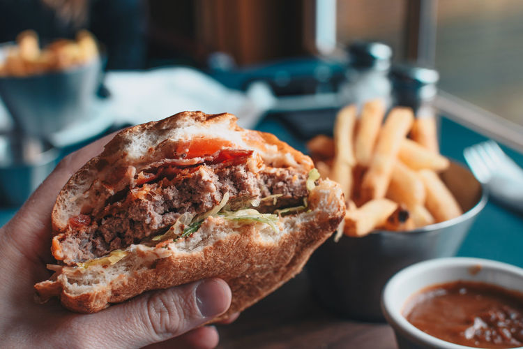 Close-up of hand holding burger in plate on table