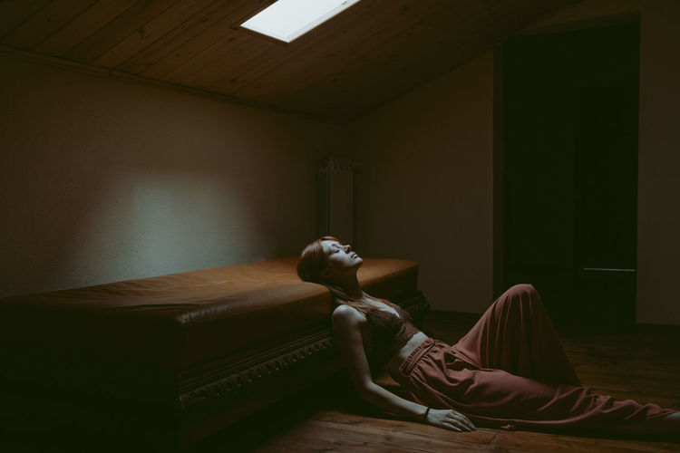 LOW SECTION OF WOMAN SITTING ON BED BY HOUSE