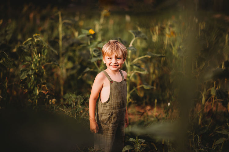Cute young boy in dungarees in a field smiling at the camera