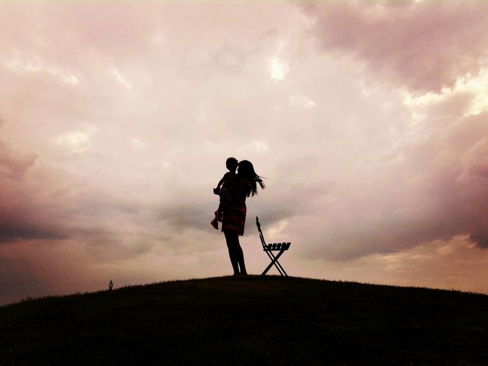 Silhouette man photographing on field against sky during sunset