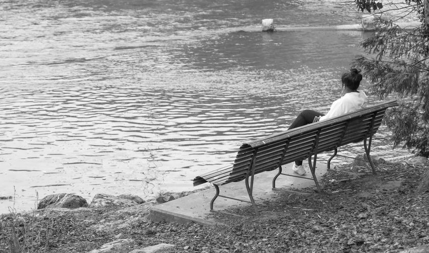 Rear view of couple sitting on bench at shore