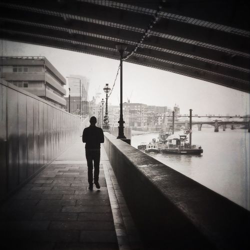 Rear view of man on river amidst city against sky