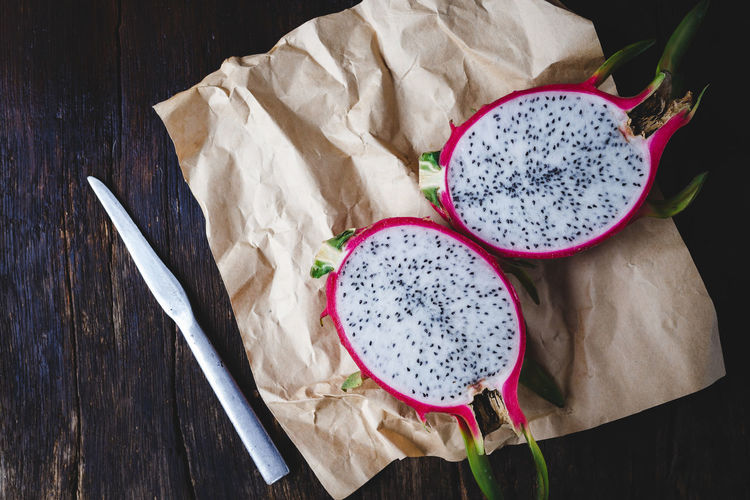 High angle view of pitaya with knife and paper on wooden table