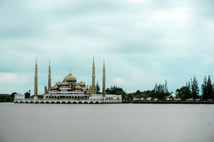 Crystal mosque by river against sky