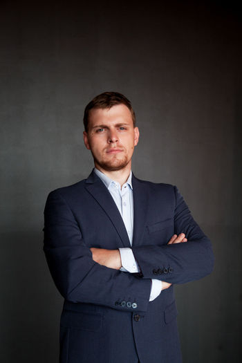 Portrait of well-dressed confident businessman with arms crossed standing against wall