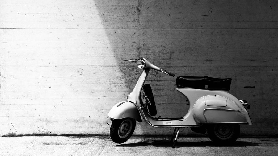 Motor scooter parked on footpath against wall