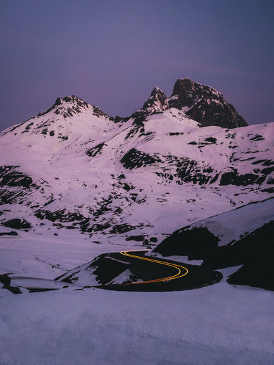 Car trails lights on road bends against snowcapped mountains, sunrise