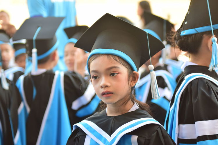 Close-up of girl wearing graduation gown and mortarboard looking away by friends