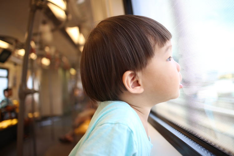 Side view of boy looking through window in train