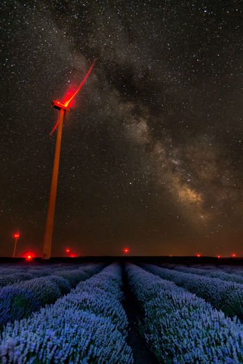 Low angle view of illuminated wind turbine on field at night