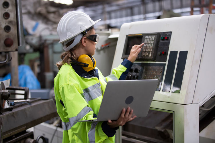 Engineer using laptop while operating machine in factory