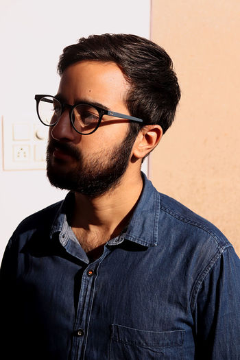 Portrait of young man wearing eyeglasses against wall