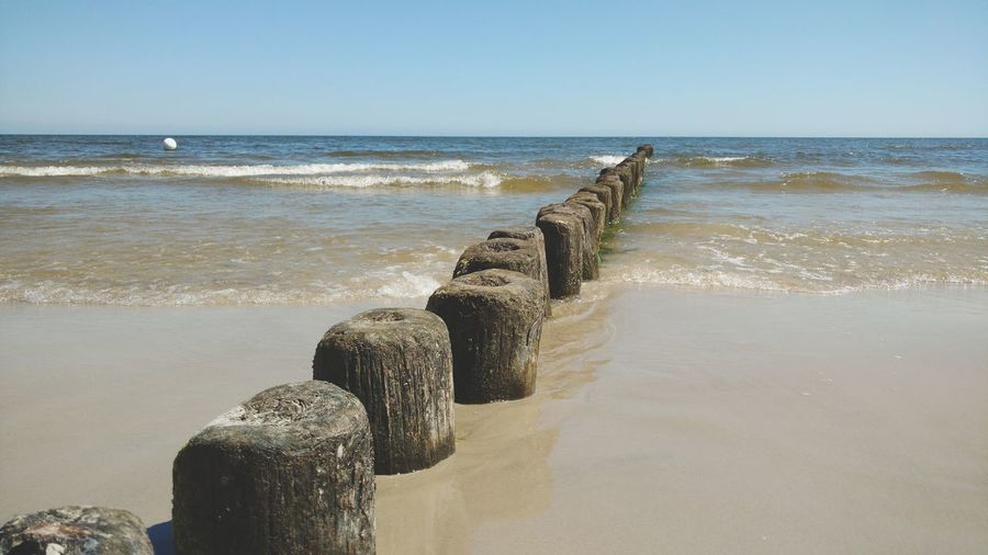Wooden posts on beach against clear sky