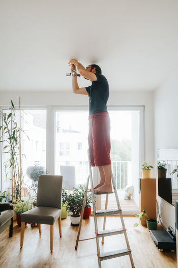 Home owner standing on ladder fixing light installation