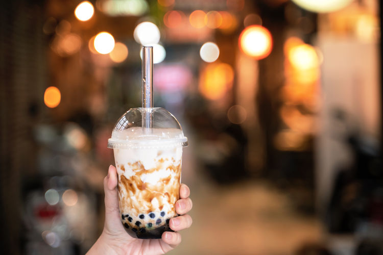 Young woman is holding, drinking brown sugar flavored tapioca pearl bubble milk tea with glass straw