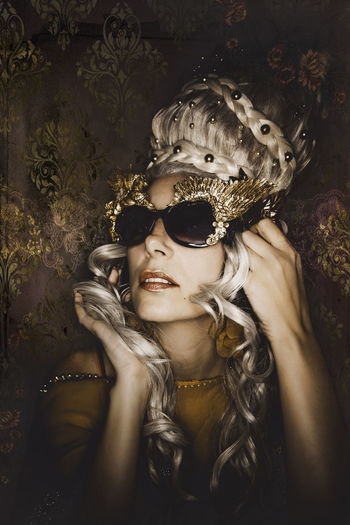 Close-up portrait of mature female model wearing sunglasses against wall
