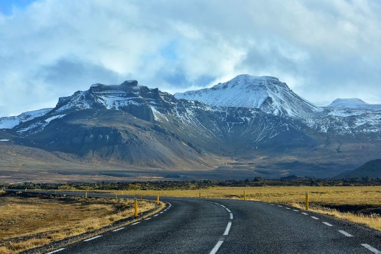 Empty road by snowcapped mountains against sky